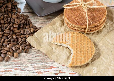 Nahaufnahme von Stroopwafelplätzchen mit einem Bissen neben Kaffeebohnen. Stockfoto