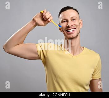 Porträt eines fröhlich freundlich lächelnden erwachsenen Mannes in gelbem T-Shirt, der seine Zähne mit einer Zahnbürste putzt. Gesunder Lebensstil Stockfoto