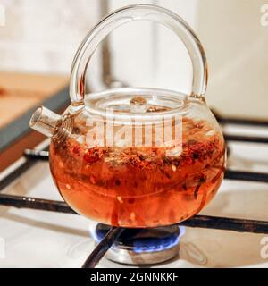 Der rote Tee wird in einem Glaskessel auf einem Gasherd in Nahaufnahme gekocht Stockfoto