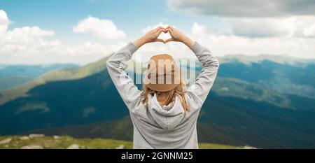 Erstaunliches Bergpanorama der Karpaten. Frau, die sich mit ihren Händen auf einem hohen Hügel in Herzform befindet. Freiheitskonzept. Rückansicht. Stockfoto