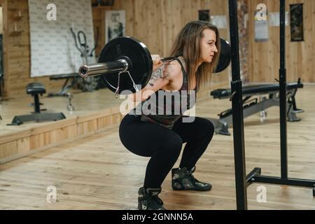 Frau, die im Fitnessstudio trainiert und Langhantelpresse macht. Hubgewicht. Schöne Frau mittleren Alters Powerlifter mit Tattoo. Stark und fit Körper, gesund Stockfoto