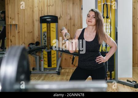 Frau, die im Fitnessstudio trainiert und Hantelpresse macht. Hubgewicht. Schöne Frau mittleren Alters Powerlifter mit Tattoo. Stark und fit Körper, gesund Stockfoto