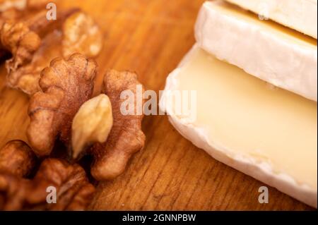 Geschnittene Kamembert- und Walnusskerne auf einem Holzschneidebrett, Nahaufnahme, selektiver Fokus Stockfoto