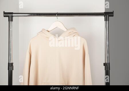 Unbeschriftete beige Unisex-Sweatshirt-Mockup auf Kleiderbügel. Kapuzenpullover im minimalistischen Innenraum. Stockfoto