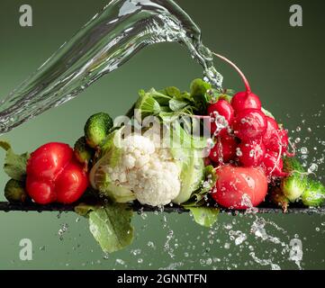 Verschiedene rohe Gemüse mit Wasserspritzer. Blumenkohl, Tomate, Gurke, Rettich und Paprika auf grünem Hintergrund. Stockfoto