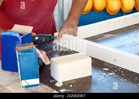 Die Hände eines Zimmermanns bohren oder Schrauben den hölzernen Dielenrahmen mit einem elektrischen Schraubendreher. Stockfoto