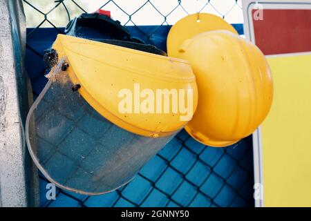 Gelbe Schutzhüte oder Schutzmütze, die in einer Reihe an einem Drahtzaun auf der Baustelle hängen. Arbeitssicherheit. Stockfoto