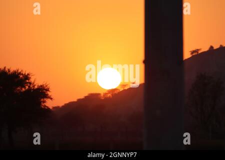 Landschaftsfoto des Sonnenuntergangs mit einem runden vollen Sonnenuntergang hinter lokalen Silhouette Bergketten und wilden Wald Silhouette Bäume und defocu Stockfoto