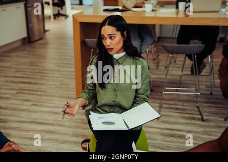 Geschäftsfrau hält Dokument im Gespräch mit Kollegen, die sich auf die Präsentation vorbereiten, sitzt in der Bürolounge Stockfoto
