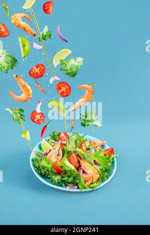 Mediterraner Salat mit Garnelen in Levitation. Frischer Gemüsesalat aus Kirschtomaten, Salat, Paprika, Garnelen auf Blau. Stockfoto