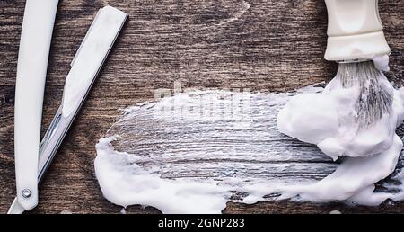 Rasierzubehör auf einem Hintergrund mit Holzstruktur. Werkzeuge. Einweg-Rasierer, Bürste, Rasierer mit Schaumgefahr. Stockfoto