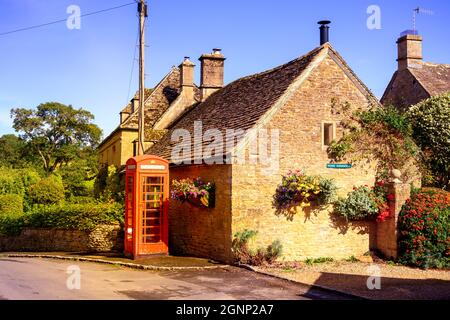 Traditionelle rote Telefonbox vor einem aus Stein gebauten Cotswold Cottage, das jetzt als Defibrillator-Lagerstation genutzt wird. Upper Slaughter Gloucestershire England Großbritannien Stockfoto