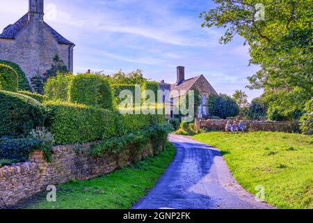 Drei ältere Frauen sitzen auf der Bank und genießen die Morgensonne im hübschen Cotswold Cotswolds-Dorf Upper Slaughter Gloucestershire, Großbritannien Stockfoto