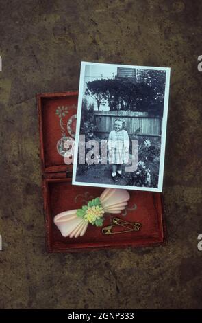 Kleine Holzkiste mit Haarrutsche und Knöpfen aus den 1950er Jahren und Sicherheitsnadeln mit Foto eines jungen Mädchens im Garten Stockfoto