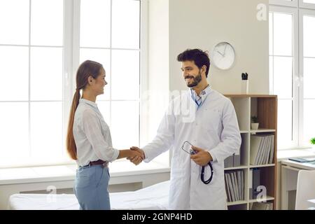 Ein freundlich lächelnder männlicher Arzt begrüßt und schüttelt die Hand des Patienten während des Treffens in der Arztpraxis. Stockfoto