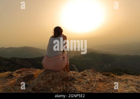 Rückansicht Porträt einer Frau, die allein den Sonnenuntergang im Berg betrachtet Stockfoto