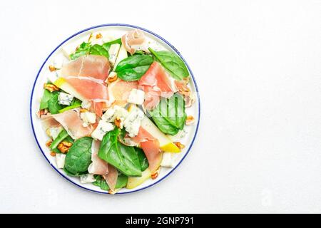 Birnensalat mit Prosciutto, Blauschimmelkäse, Spinat, Walnüssen auf weißem Hintergrund, Draufsicht, Kopierraum Stockfoto