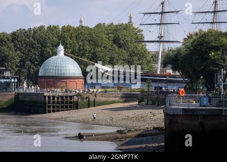 Ein Mann geht am 16. September 2021 am Ufer der Themse in der Nähe des Frachtklippers Cutty Sark entlang, dessen hohe Masten in der Nähe des südlichen Eingangs des Greenwich Foot Tunnels und der Doppelkuppeln des Greenwich Hospital in London, England, zu sehen sind. Stockfoto