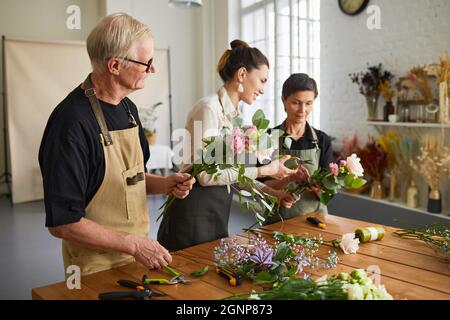 Portrait einer lächelnden Frau Floristin, die reifes Paar lehrt, Blumenkompositionen in der Werkstatt zu arrangieren Stockfoto