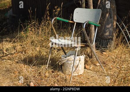 Ein rostiger Stuhl und ein weißer Plastikeimer, der auf einem Feld abgelegt wurde (Umbrien, Italien, Europa) Stockfoto
