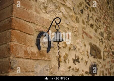 Eine schmiedeeiserne Glocke an der Wand eines Steingebäudes (Umbrien, Italien, Europa) Stockfoto