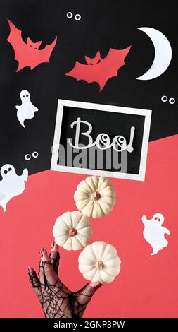 Abstrakte Halloween Komposition in rot, schwarz und weiß. Text Boo auf Tafel. Papiersilhouetten von Mond, Fledermäusen, Geistern, Augen. Handstützen Pyramide Stockfoto