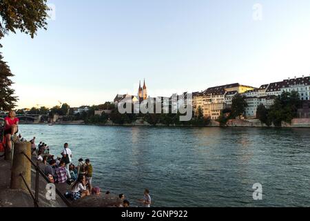 Basel, Schweiz - 24.09.21. Rheinboulevard mit Blick auf die Altstadt und das Basler Münster. Menschen, die sich am Flussufer entspannen. Stockfoto