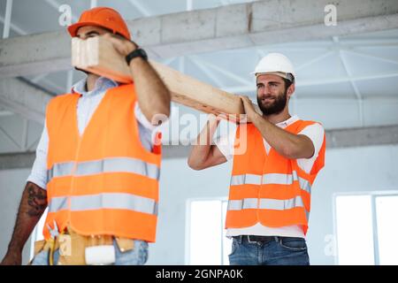 Zwei junge Bauherren, die Holzbretter auf der Baustelle trugen, aus der Nähe Stockfoto