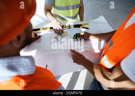 Nahaufnahme von drei Mann-Ingenieuren, die sich die Blaupause auf der Baustelle angeschaut haben Stockfoto