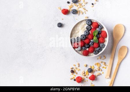 Hausgemachtes Müsli auf einem weißen Teller mit Beeren und Früchten. Ein gesundes Frühstück, eine Quelle von Eiweiß und nützlichen Substanzen. Grauer Hintergrund, Draufsicht. Stockfoto