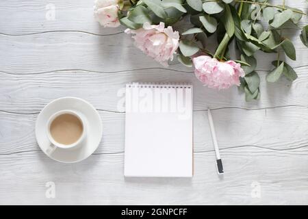 Leeres offenes Notizbuch und eine Tasse Kaffee mit Blumen auf dem Schreibtisch/Flat Lay. Stockfoto