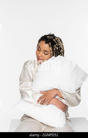 Verschlammen und lächelnd afroamerikanische Frau umarmt Kissen auf weiß Stockfoto