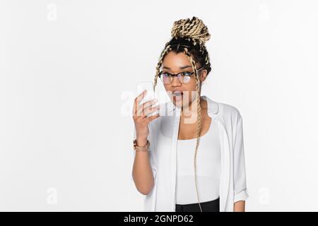 Erstaunt afroamerikanische Geschäftsfrau in Brillen Blick auf Mobiltelefon isoliert auf weiß Stockfoto