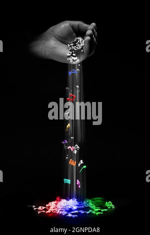 Mehrfarbige Musiknoten, die aus der Hand auf schwarzem Hintergrund fließen. Das Konzept des Erschaffens, Improvisierens und Spielens von Musik Stockfoto