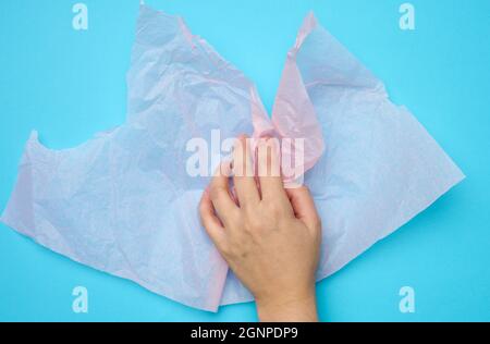 Weibliche Hand halten rosa gefaltet Verpackung zerknittertes Papier auf einem blauen Hintergrund Stockfoto