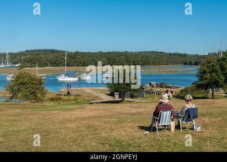 Menschen sitzen und genießen einen sonnigen Tag beobachten die Boote und Yachten auf Beaulieu River von Bucklers Hard Dorf im New Forest, Hampshire, Großbritannien Stockfoto