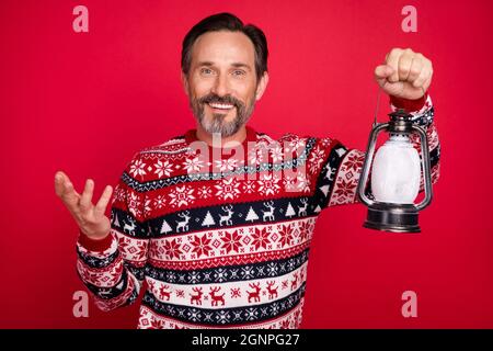 Foto Porträt Mann lächelnd in Pullover halten weihnachtslaterne isoliert lebendige rote Farbe Hintergrund Stockfoto