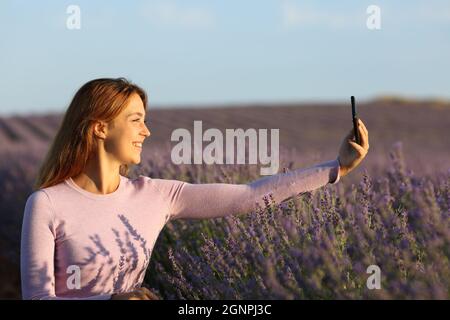 Profil einer glücklichen Frau, die bei Sonnenuntergang Selfie mit dem Smartphone im Lavendelfeld macht Stockfoto