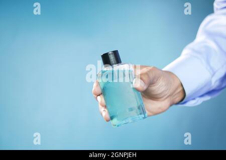 Halten Sie einen Mundspülbehälter mit der Hand auf blauen Hintergrund Stockfoto
