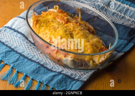 Nahaufnahme des Abendessens in einer Auflaufform mit Hühnchen-Enchiladas, garniert mit Enchilada-Sauce und Käse Stockfoto