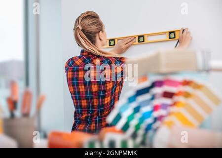 Pretty Woman doing Repair with Level Ruler near the Wall. Neue Farben Für Die Wohnung Wählen. Professionell bei der Arbeit. Stockfoto