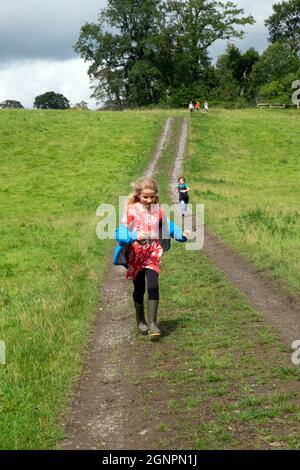 Kinder glückliches Mädchen, das im Sommer im Dinefwr Park Llandeilo Carmarthenshire Wales UK auf einer ländlichen Strecke auf einem Familienspaziergang läuft. KATHY DEWITT 2021 Stockfoto