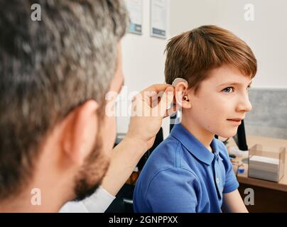 Hörbehandlung für ein Kind. Kaukasischer Junge während der Installation Hörgerät durch Audiologe in Hörklinik Stockfoto