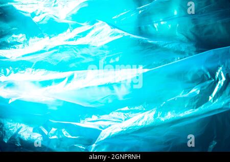 Abstrakter Hintergrund aus blauer Plastiktüte und hintergrundbeleuchtetem Blitzlicht. Grunge-Textur. Lebendige Farben. Minimaler Hintergrund und Umweltverschmutzung. Stockfoto