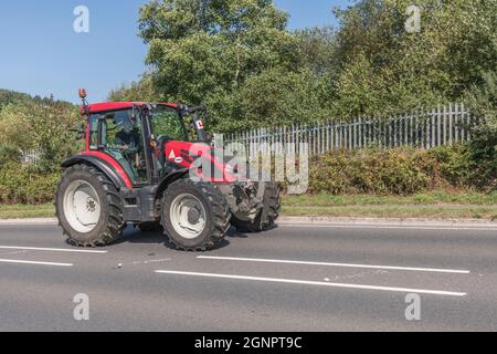 Vorne 3/4 Profil des roten Valtra Traktor auf offener bergauf Landstraße. Valtra ist eine finnische Traktormarke, dies ist das Modell der G-Serie G136. Stockfoto