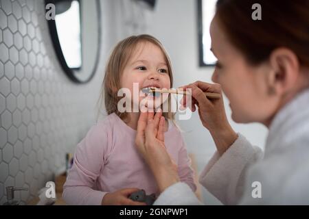 Mutter mit kleiner Tochter, die abends oder morgens im Badezimmer Zähne putzt. Stockfoto