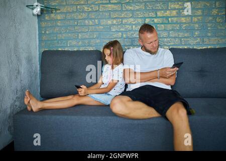 Vater und Tochter stöberten auf dem Handy, während sie sich zu Hause auf dem Sofa entspannen Stockfoto