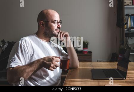 Junger Mann, der zu Hause eine Teepause nimmt. Junger Mann, der von zu Hause aus arbeitet. Stockfoto