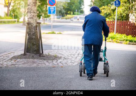 Rückansicht einer alten Person, die an einem sonnigen Tag mit einem Rollator auf der Straße läuft Stockfoto