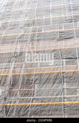 Baustelle mit einem Schutznetz an der Fassade eines Gebäudes mit Gerüsten. Altes Wohnhausrenovierungskonzept. Vertikale Ansicht Stockfoto